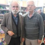 Unë dhe Prend Ndue Buzhala, në Panairin e Librave, në Tiranë, Shqipëri, pranë stendës së Akademisë Alternative Shqiptare Rrënjët tona me librat e mia.